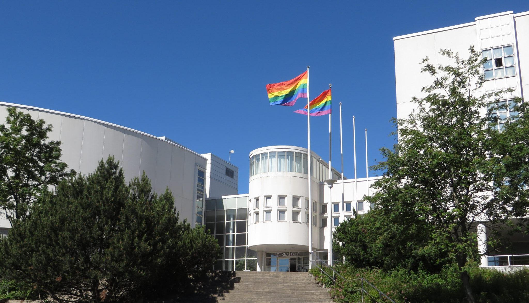 Kaksi pride-lippua liehuu salossa Valkean Talon edustalla kesällä. 