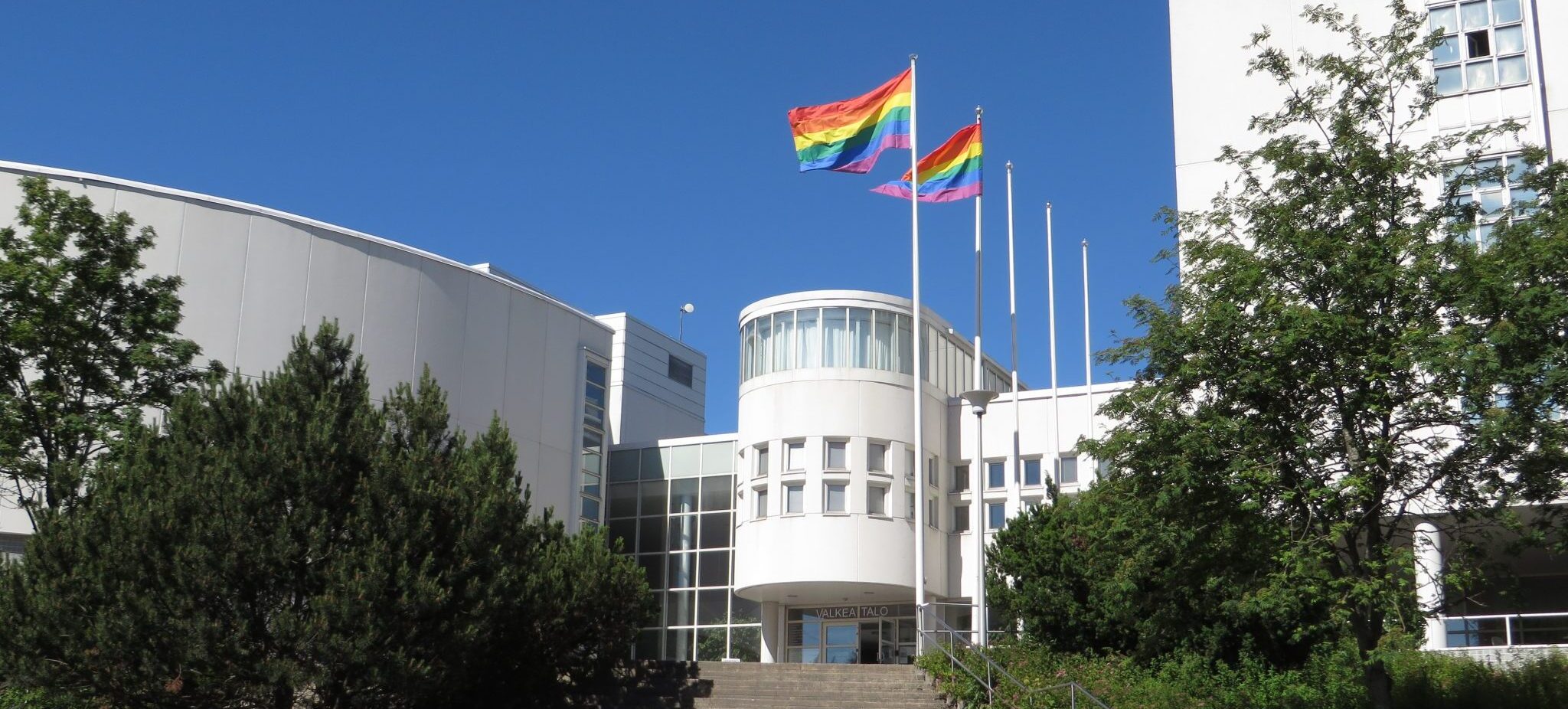 Kaksi pride-lippua liehuu salossa Valkean Talon edustalla kesällä. 