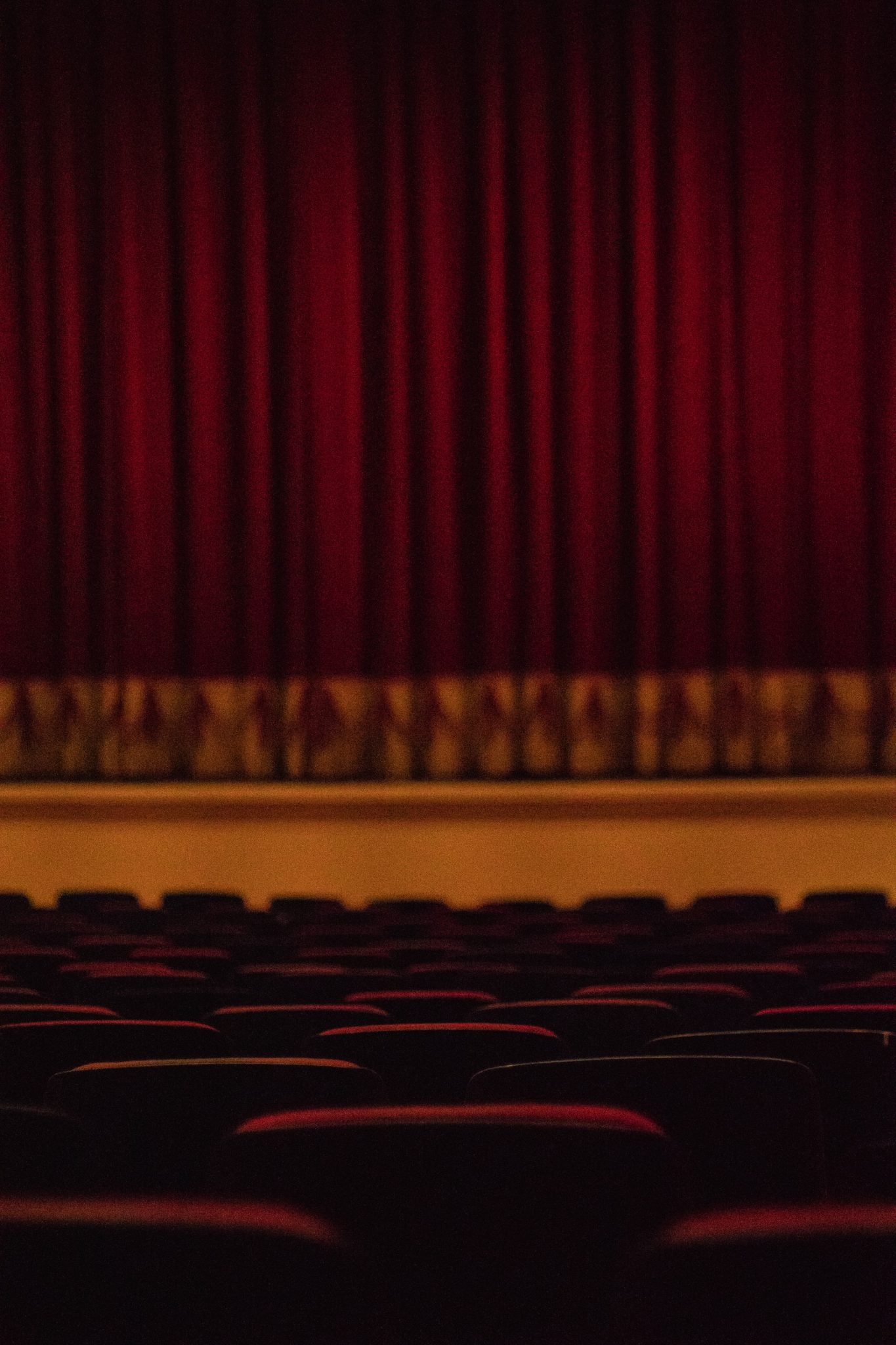 Kuvassa tyhjä teatterisali, jossa näkyy tyhjiä tuoleja sekä teatterin esirippu.