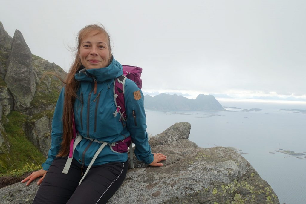 Nuori nainen hymyilee istuessaan korkean vuoren reunalla Norjan vuoristossa Lofotenilla.