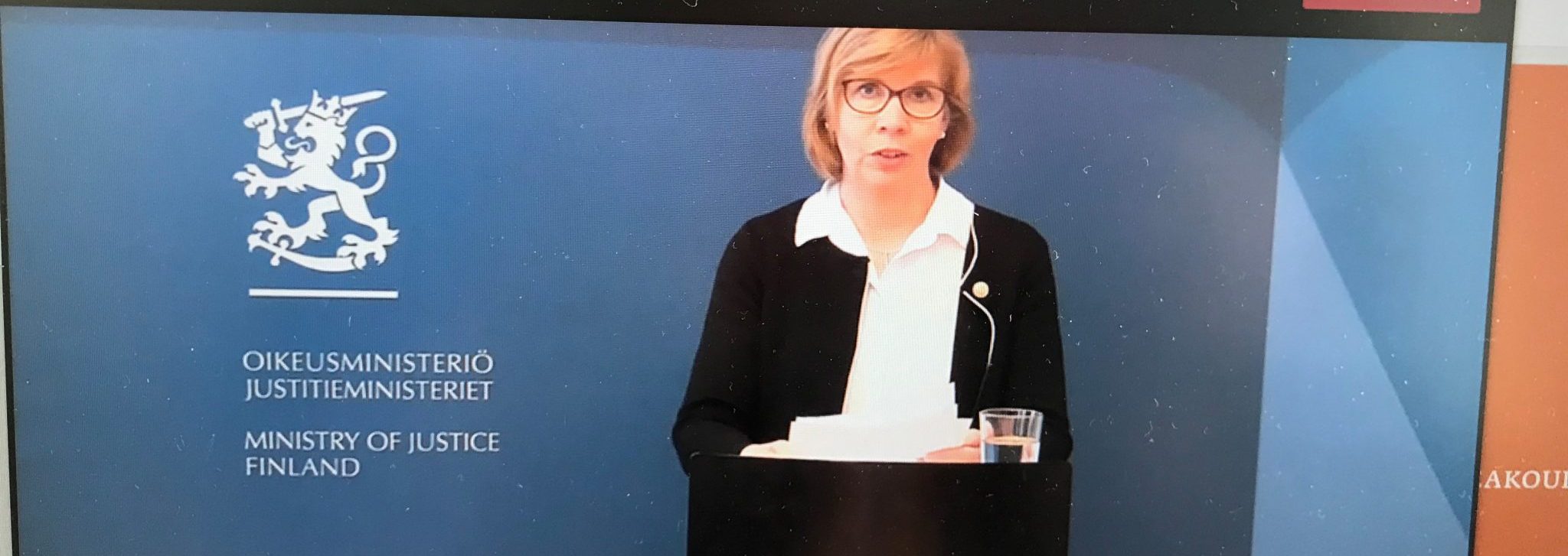 Oikeusministeri pitää puhetta puhujapöydän takaan, taustalla sininen seinä ja Suomen vaakuna.