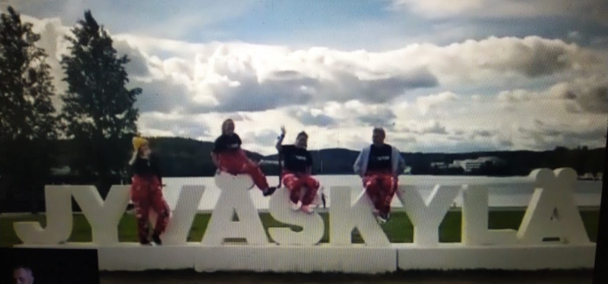 Videokaappauskuva Jyväskylä tutorit punaisissa haalareisa ja verryttelytakeissa, taustalla pilvinen taivas.