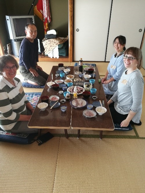 Four people sitting on their knees around a Japanese table on pillows. The table is filled with food. 