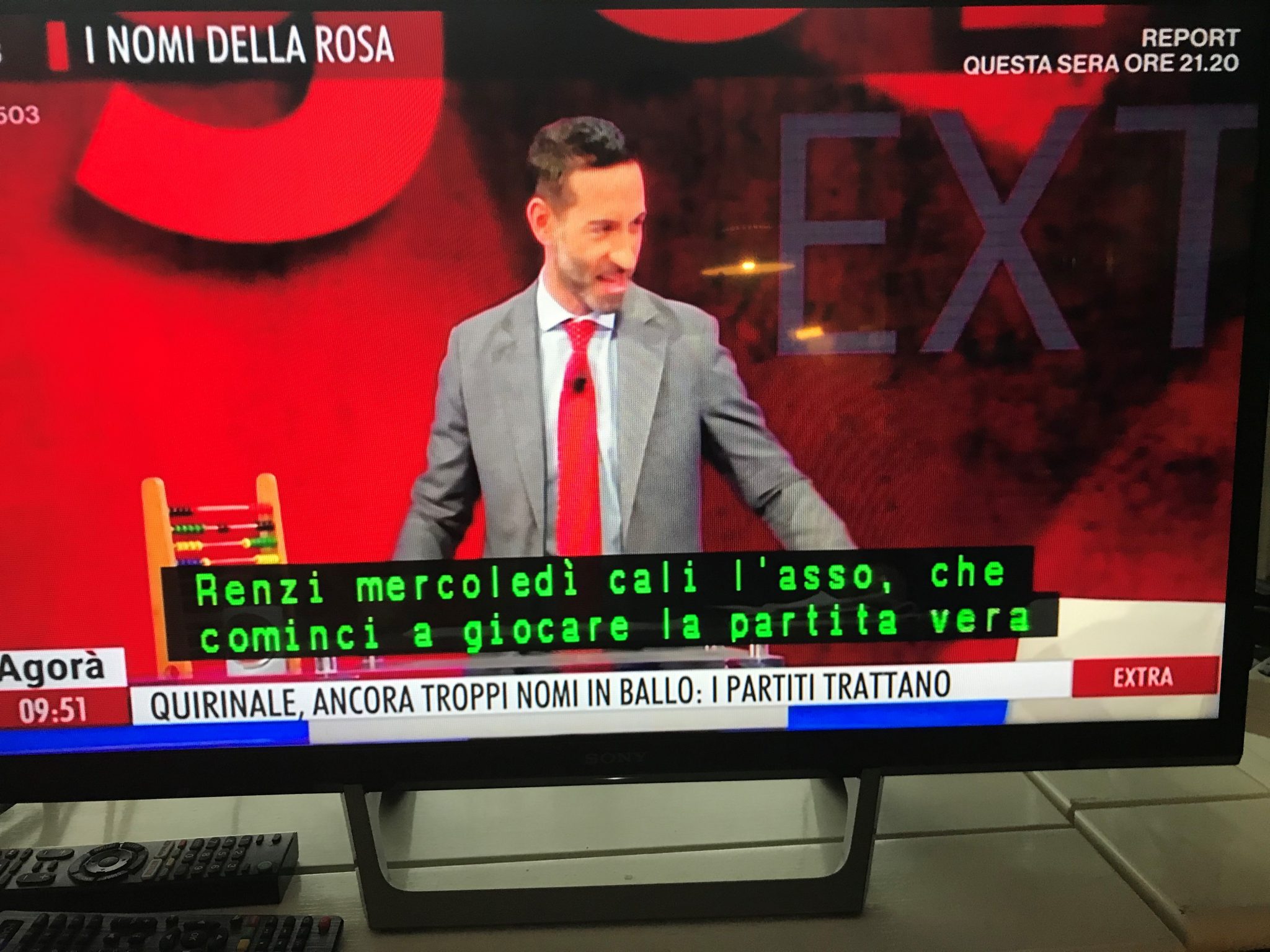 TV-ruudussa miesjuontaja, joka katsoo sivuun. Alalaidassa kaksirivinen teksti toistaa haastateltavan italiankielistä puhetta.