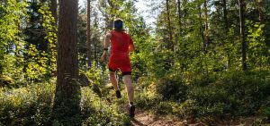 A person wearing orange sportswear and a fitness watch is trail running in a forest.