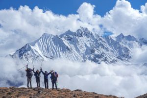 Neljä ihmistä seisoo lumisen vuorenhuipun edessä rinkkojen ja aurinkolasien kera.