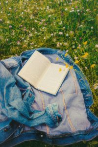 Farkkutakki ja avoinna oleva kirja kesäisellä nurmikolla.