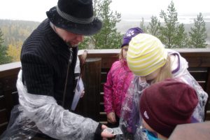 A man wearing a slouch hat teaching children how to use a compass.