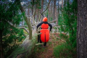 Nainen seisoo metsässä punamustassa koppakuoriaspuvussa kuvattuna takaapäin.