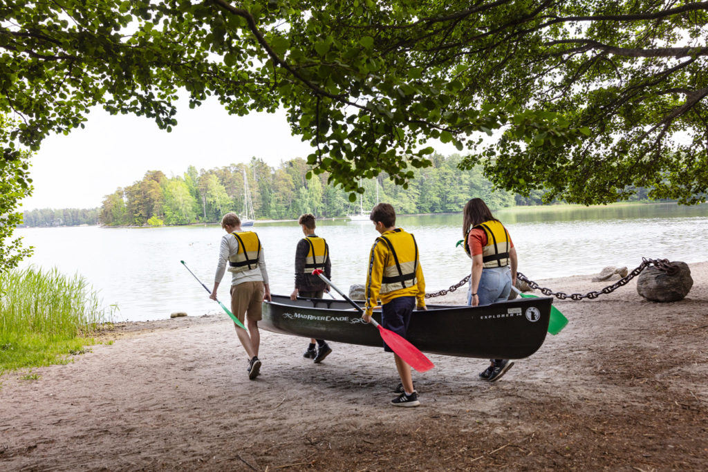 Neljä henkilöä kantaa kanoottia järven rantaan.