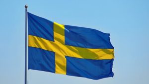 The Swedish flag on a flagpole against the light blue sky.