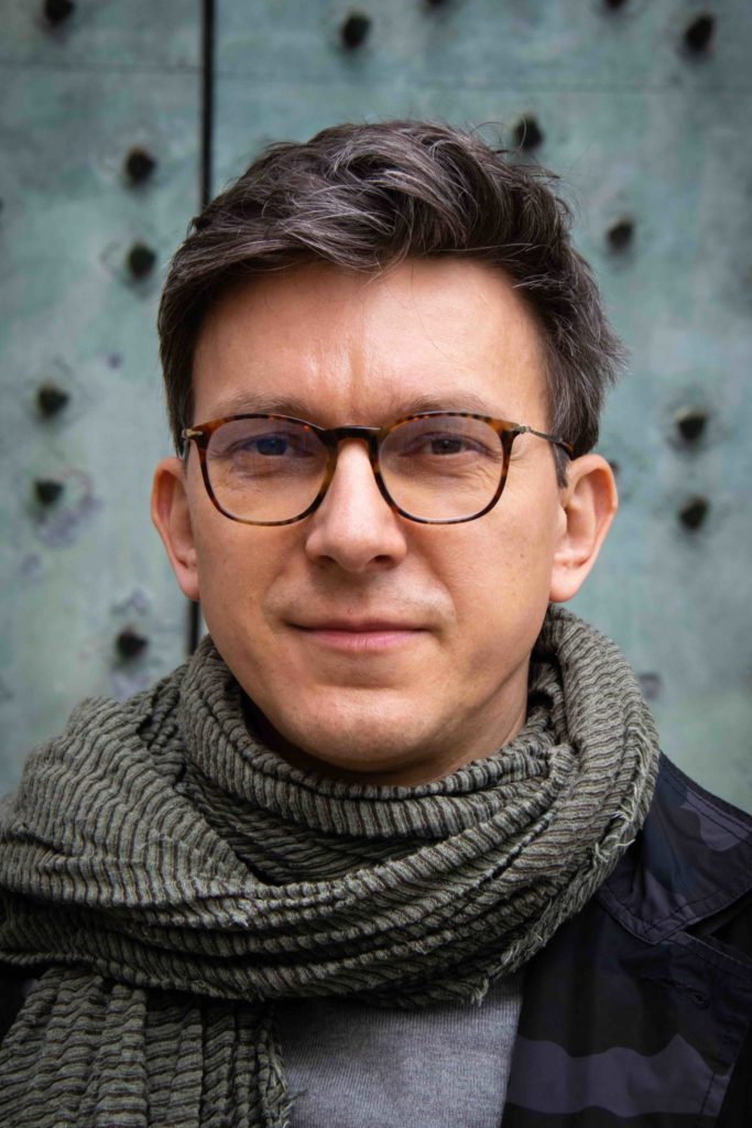 Portrait of a dark haired man with a glasses.