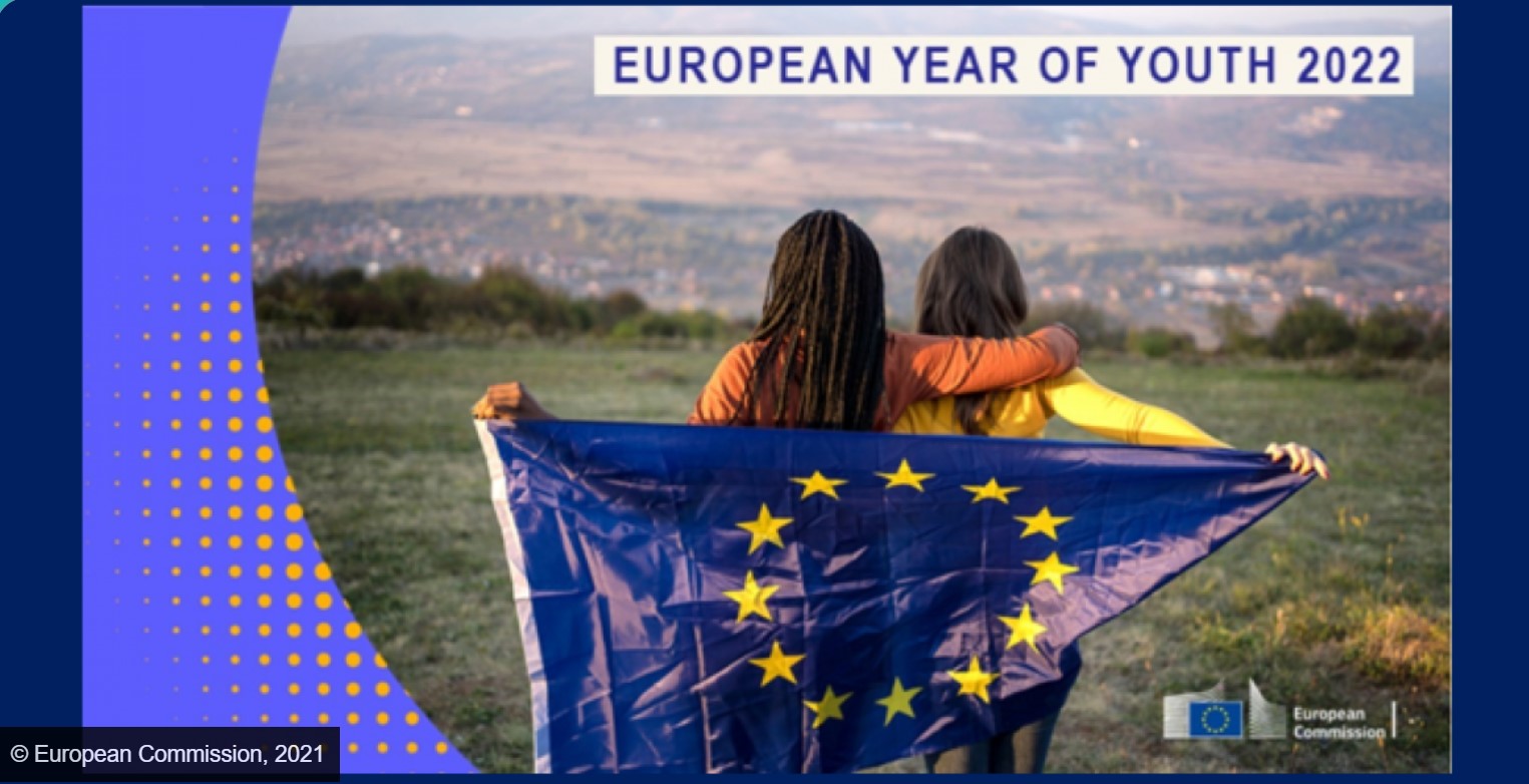 two young people standing side by side looking at the landscape, each holding the European Union flag with one hand
