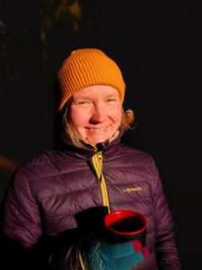 Miia Riihimäki, Nainen toppatakissa hymyilee pipossa ja villakäsineessä oikeassa kädessa on muki.