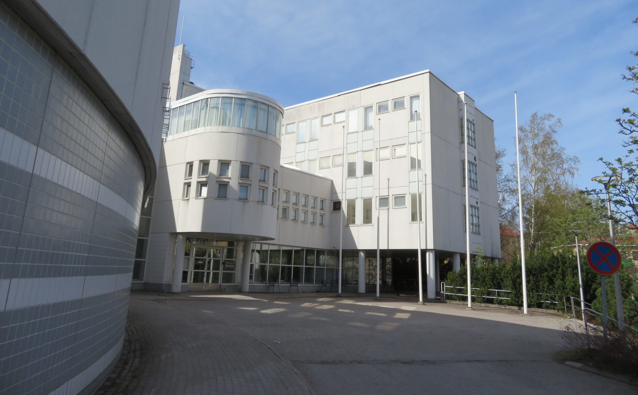 Valkea Talo, Humakin Helsingin kampus Haagassa, ulkokuva rakennuksesta, jossa eri muotoisia rakenteellisia osia ja piha-aluetta, jossa myös puita.