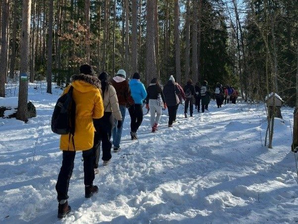 Opiskelijat kävelevät lumisessa metsässä.