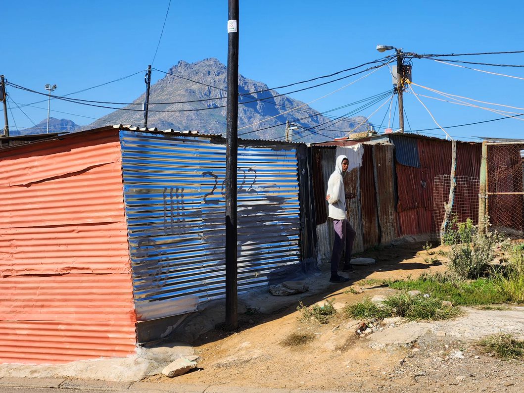 aaltopellistä tehtyjä rakennuksia ja nuori mies Stellenboschin köyhällä asuinalueella. 