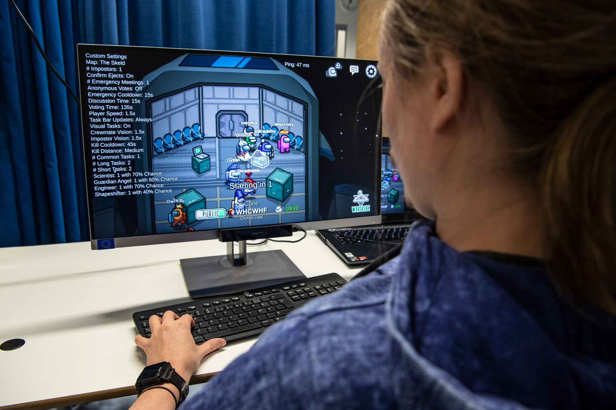 Kuvassa mies pelaa Among Us-peliä tietokoneella selkä kameraan päin. Tietokoneen näytöllä näkyy pelinäkymä ja pelihahmoja.