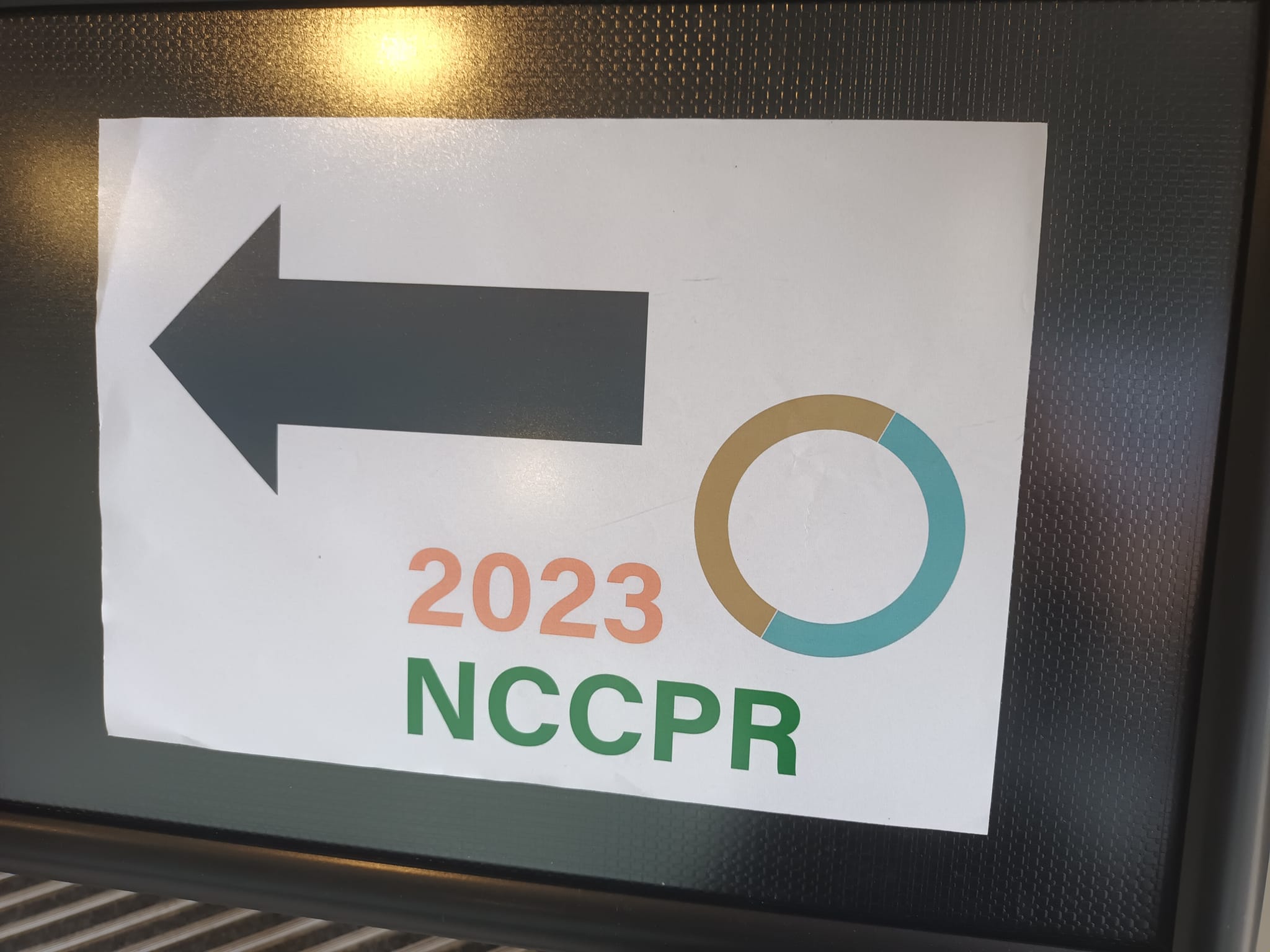 Kuvassa taulu, jossa teksti: 2023 ja sen alla kirjaimet, NCCPR. Oikeassa yläkulmassa renkaan kuva ja vasemmalla vasemmalle suuntaava paksu nuoli.