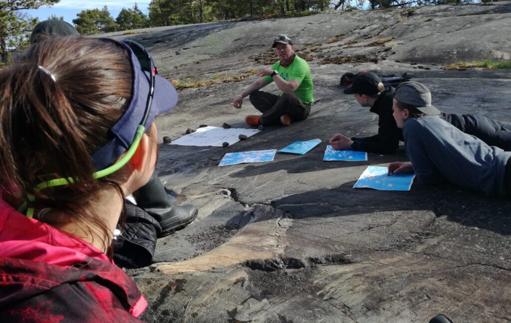 A lecturer teaching navigation outdoors on a cliff to students.