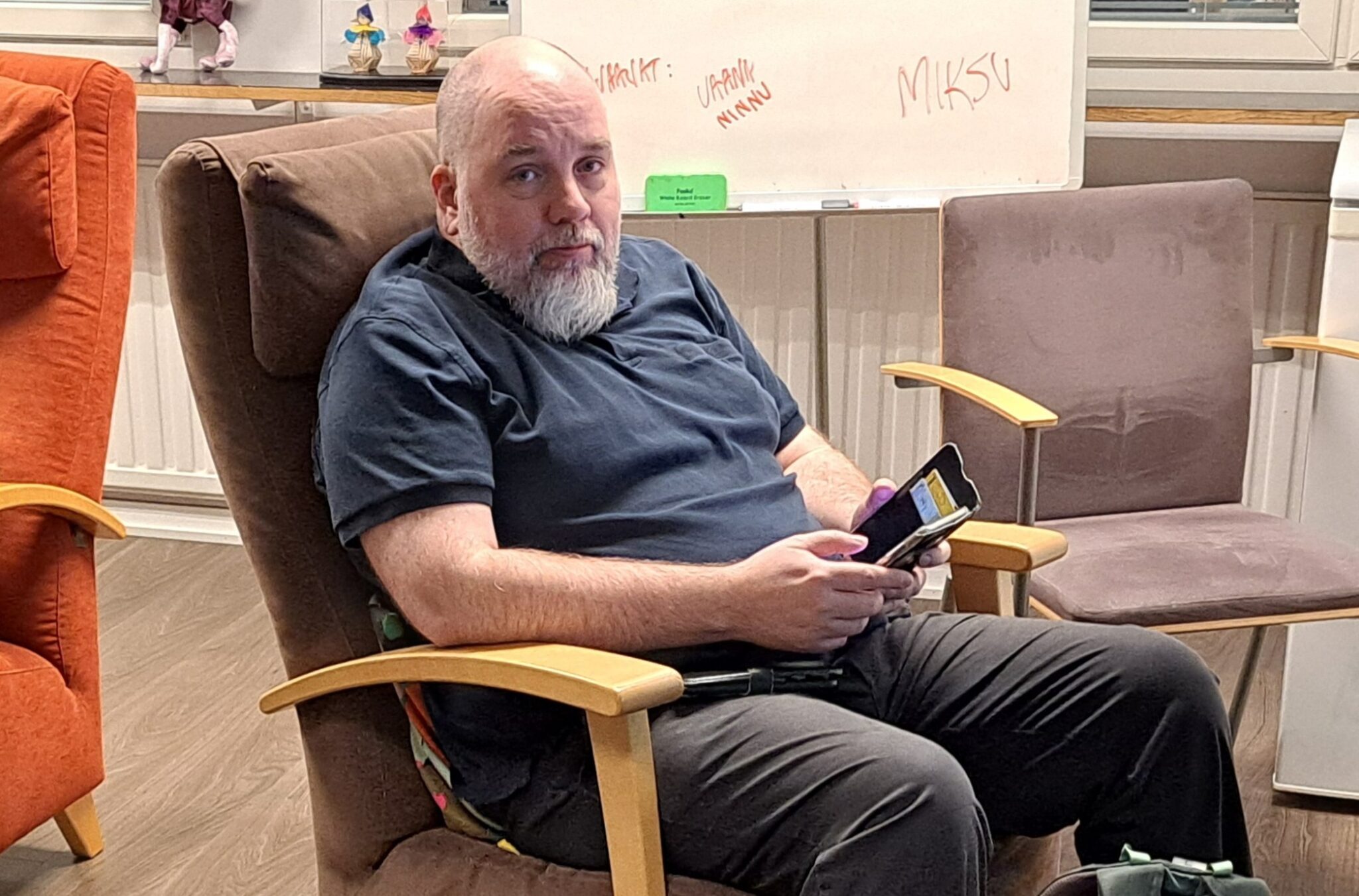 Mieshenkilö istuu nojatuolissa ja hänellä on matkapuhelin kädessään.