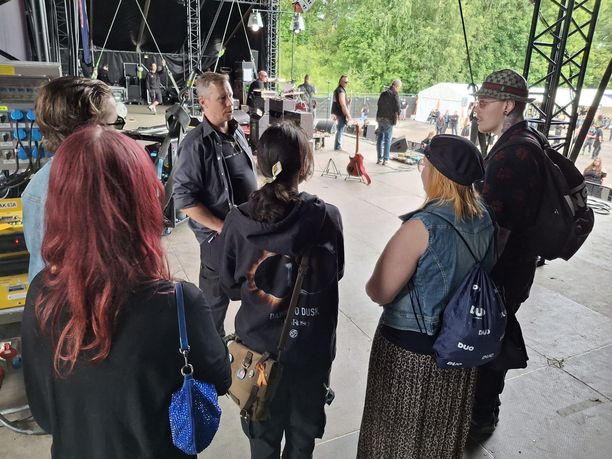 Viisi nuorta seisoo ringissä esiintymislavan sivussa ja kuuntelee aikuista.