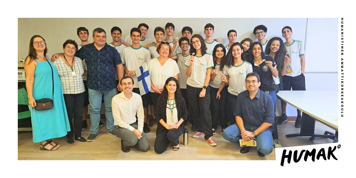 Suuri ryhmä ihmisiä seisoo ja katsoo kameraan. Mukana on myös Suomen lippu