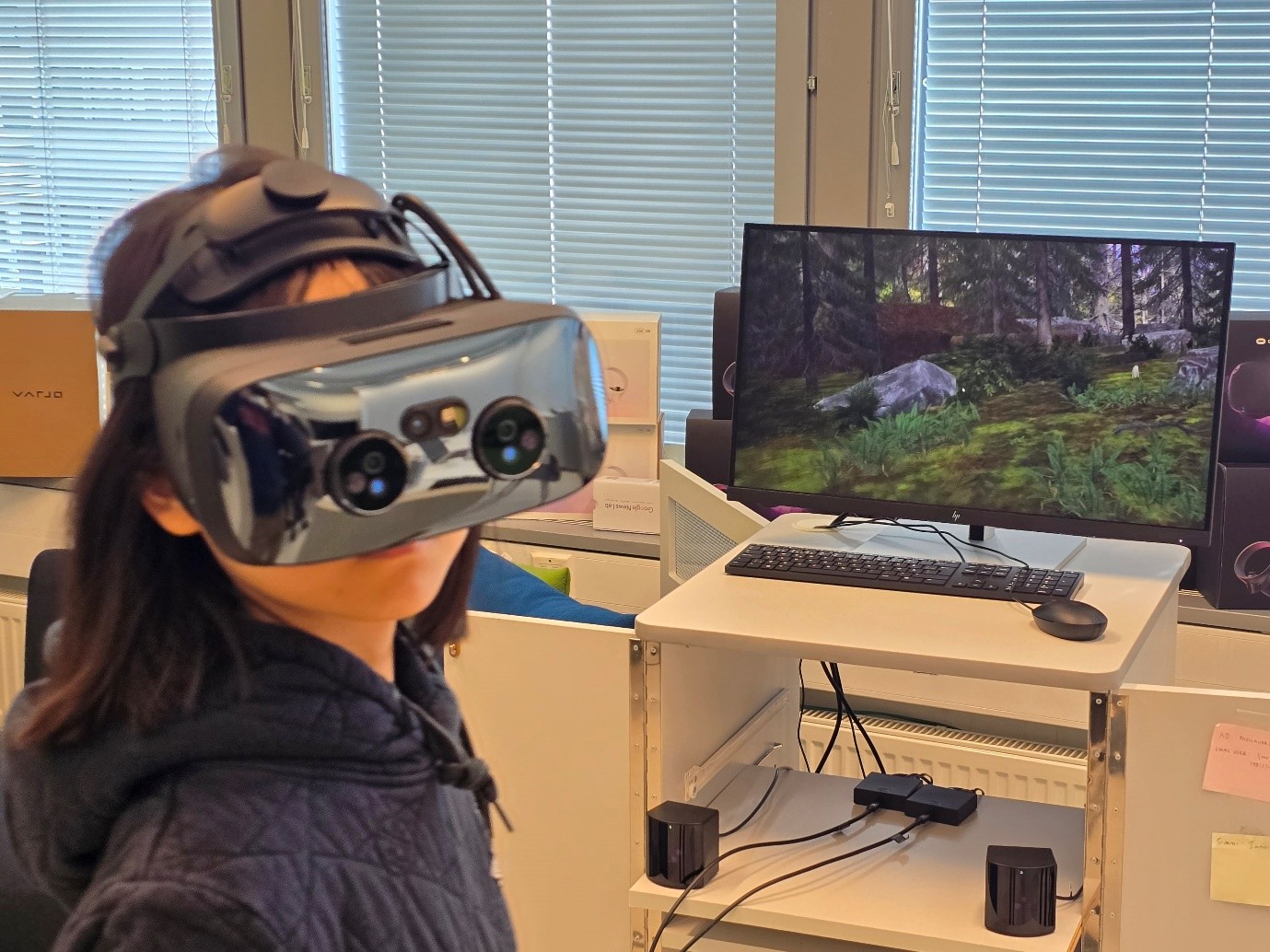 Kuva henkilöstä pitämässä esitelmää. Taustalla esitelmän ensimmäinen dia. Etualalla kuuntelijoita keskustelemassa keskenään.