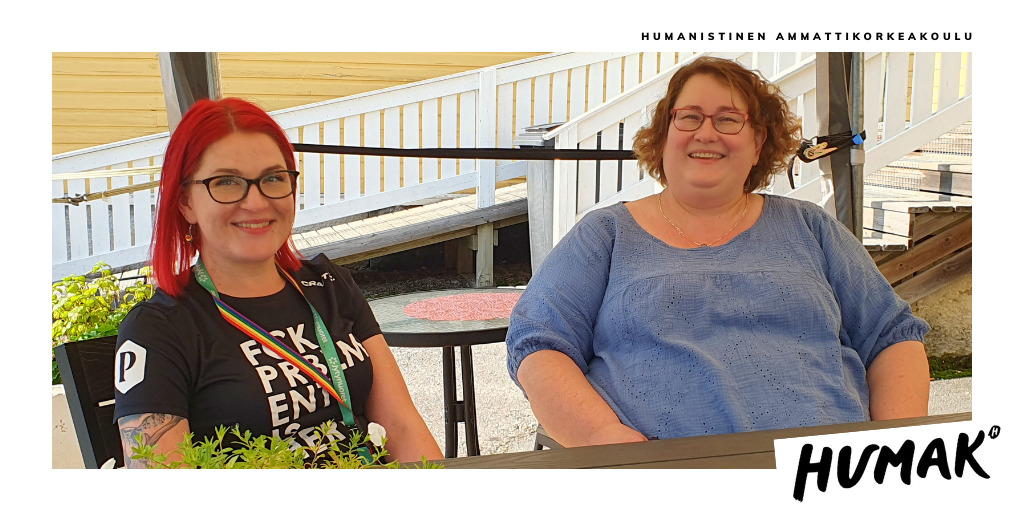  Kaksi henkilöä (Ansku Kumpulainen ja Liisa Raatikainen) istuvat ulkona auringonpaisteessa pöydän ääressä.&nbsp;