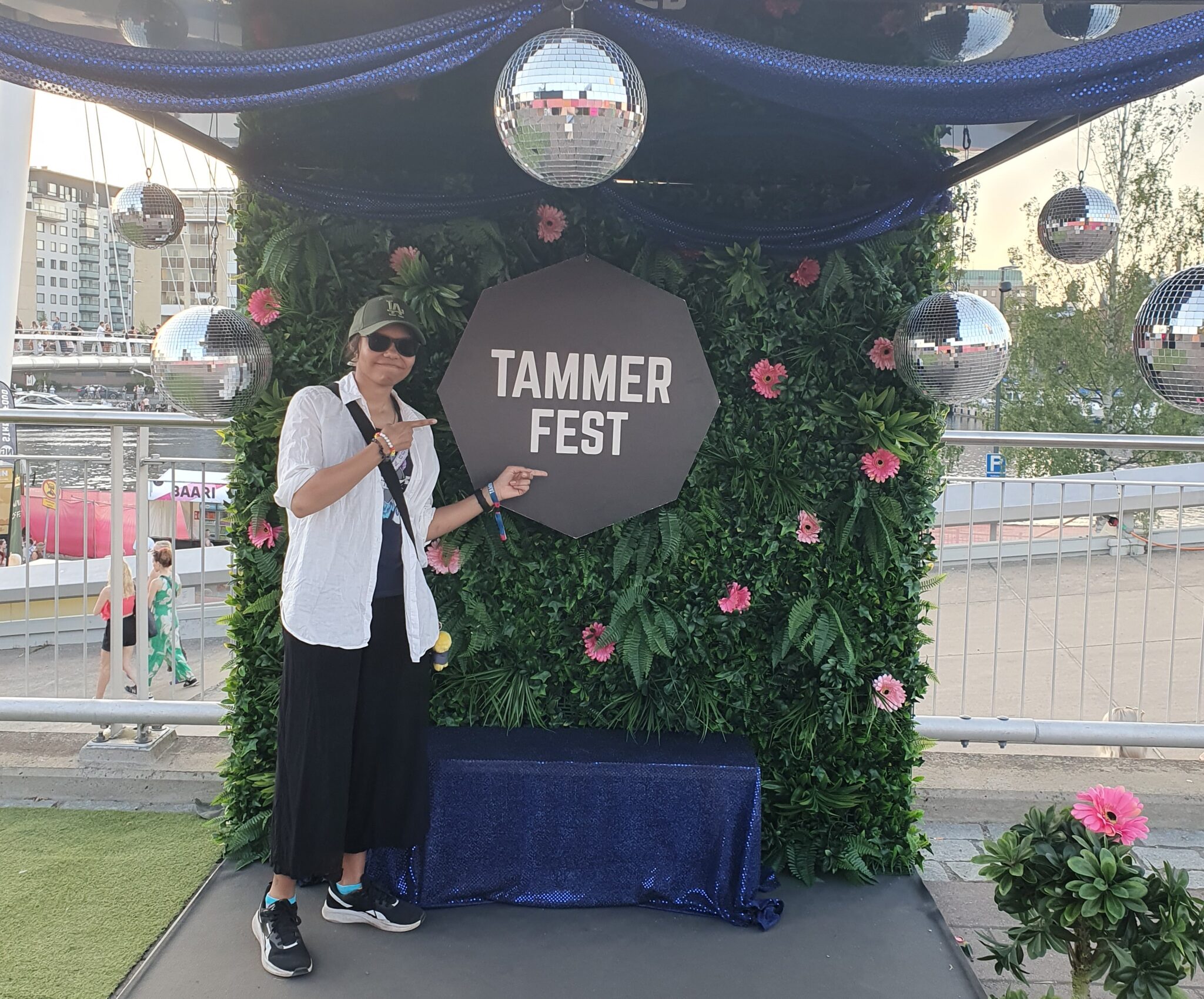 Lippalakkipäinen ja hymyilevä nuori seisoo festivaalin kukikkaan kuvausseinän edessä.