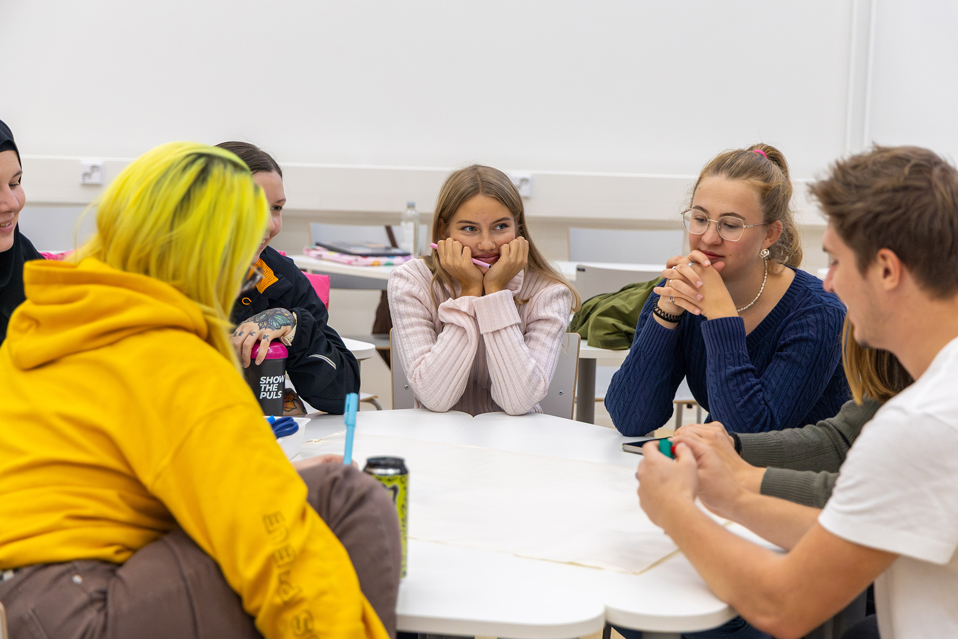 Ryhmä istuu pöydän ääressä ja keskustelee, pöydällä näkyy papereita ja juomapulloja.