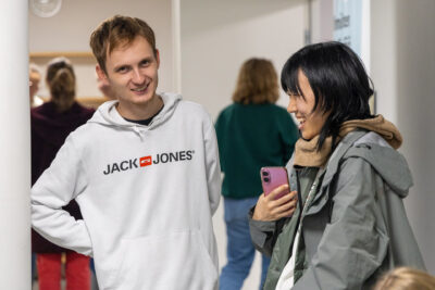 Kaksi henkilöä seisoo käytävällä ja keskustelee, toinen pitää puhelinta kädessään.