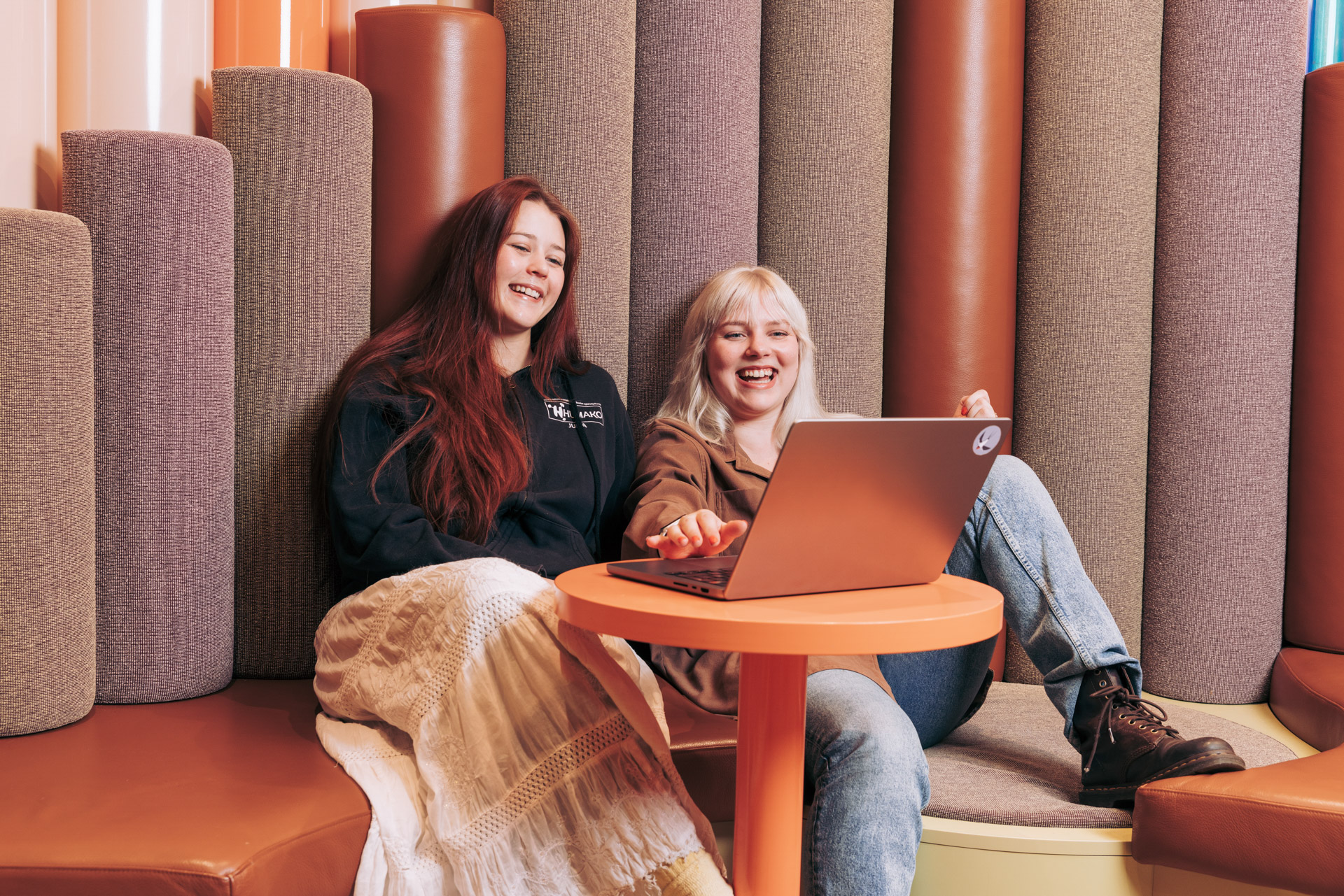 Kaksi henkilöä istuu sohvalla ja työskentelevät yhdessä kannettavan tietokoneen äärellä, joka on pöydällä. Henkilöt nauravat.