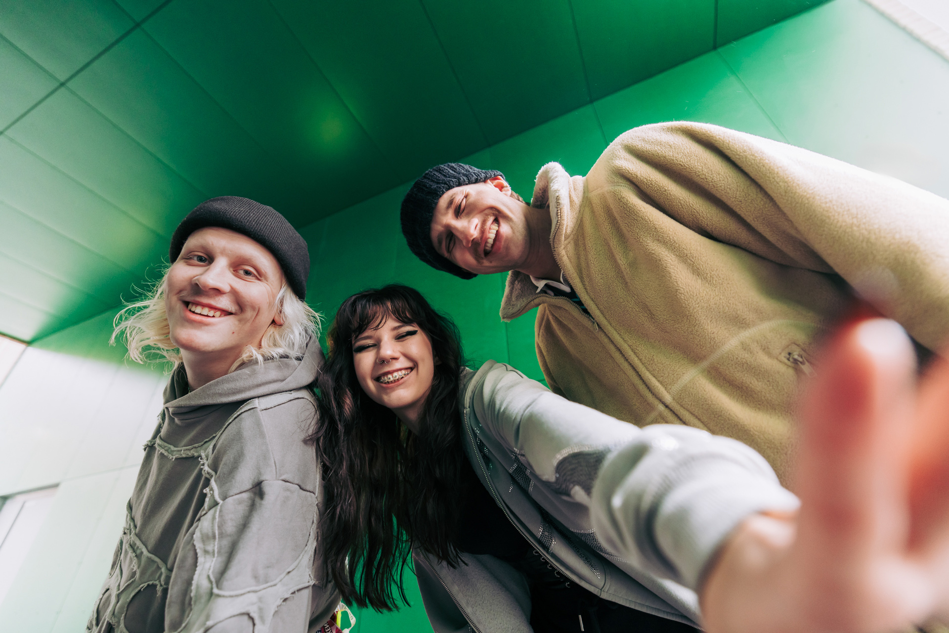 Kolme henkilöä katsoo iloisesti kohti kameraa. Taustalla vihreää seinää.