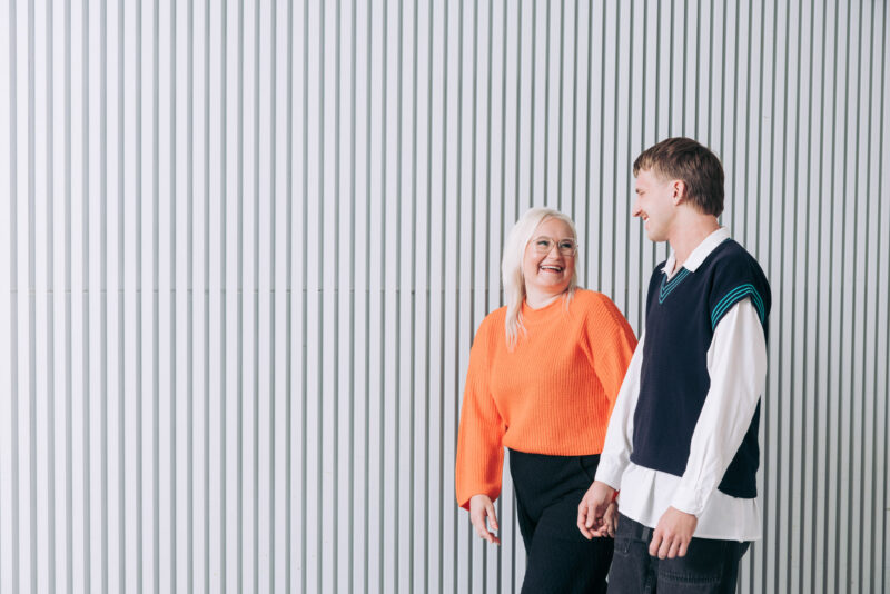 Kaksi henkilöä kävelee rinnakkain modernin rakennuksen seinän vieressä ja keskustelee.