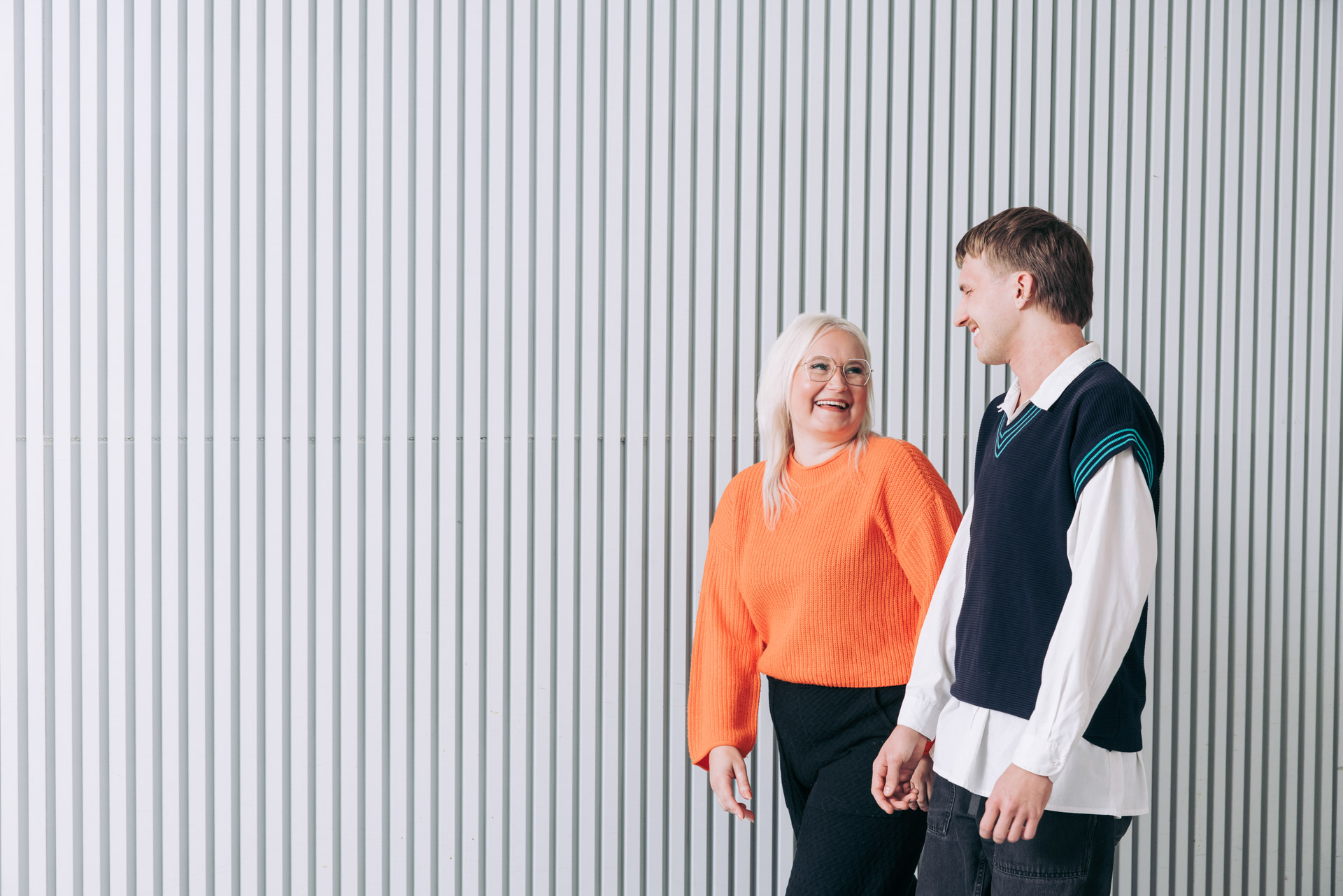 Kaksi henkilöä kävelee rinnakkain modernin rakennuksen seinän vieressä ja keskustelee.