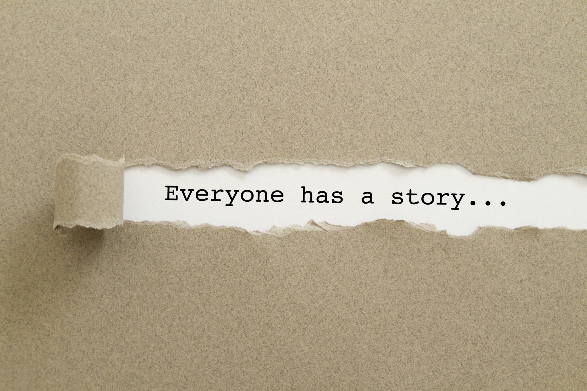 Pahvialusta, jonka repäistyn pintakerroksen alla lukee “Everyone has a story”