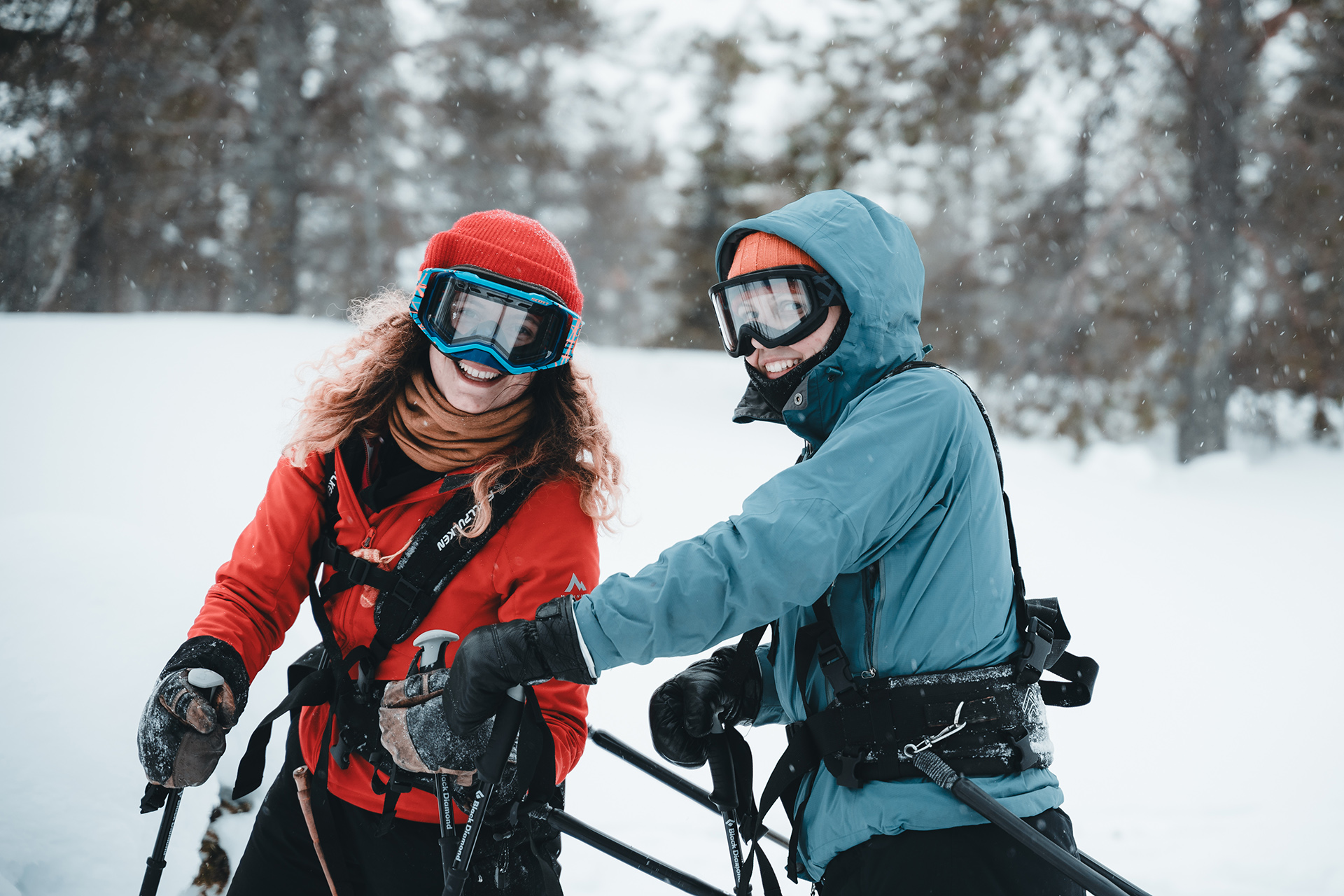 Kaksi henkilöä seisoo lumisessa maastossa kiipeilyvarusteissa ja köysissä, taustalla näkyy puita ja lumisade.