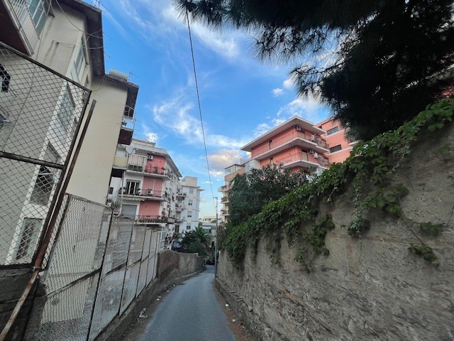 A narrow old street with a wall on one side and residential houses around.