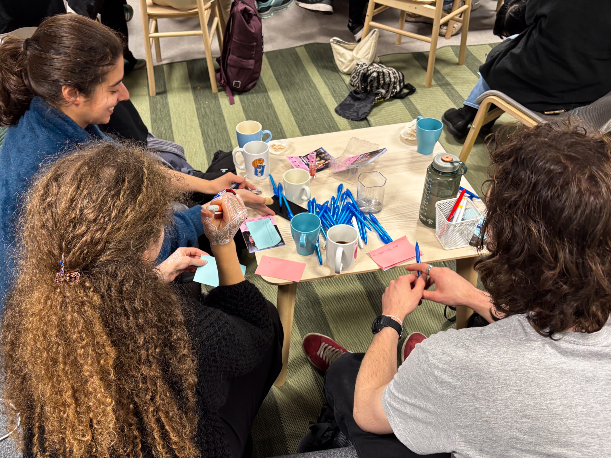 Students sitting on a couch write ideas on Post-it notes together while having coffee.