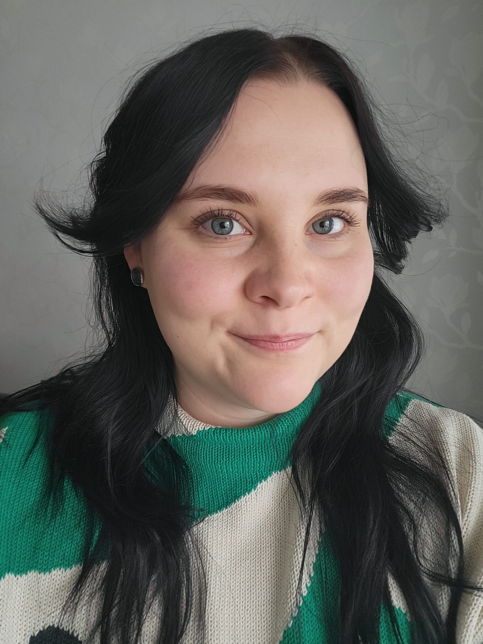 Kasvokuva naisesta, jolla on pitkät, tummat hiukset ja siniset silmät. Hän hymyilee hennosti kameralle. Hänellä on yllään vihreän ja kermanvärinen raidallinen neule.