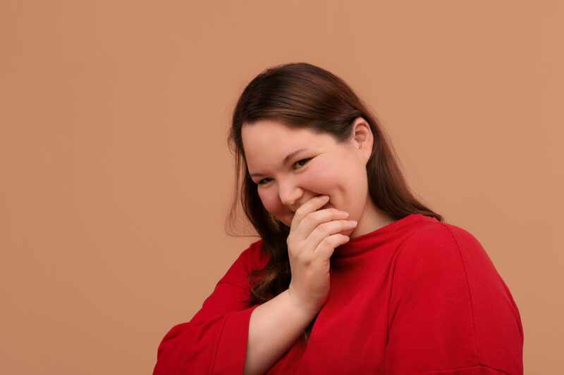 Tummahiuksinen henkilö hymyilee vienosti ja pitää kättään kasvojensa edessä.