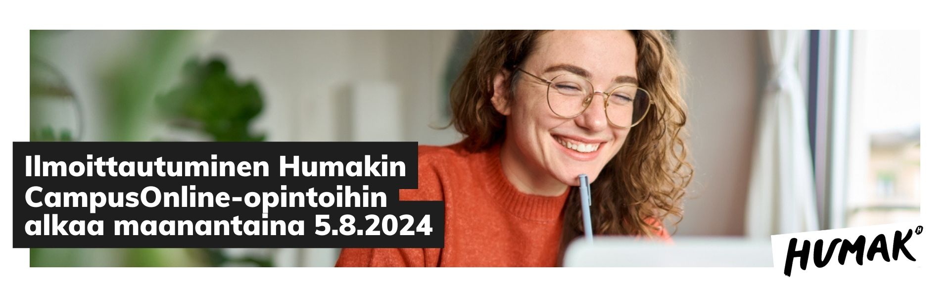 Punatukkainen, tiilinpunaiseen paitaan pukeutunut silmälasipäinen nainen katsoo hymyillen läppärinsä ruutua