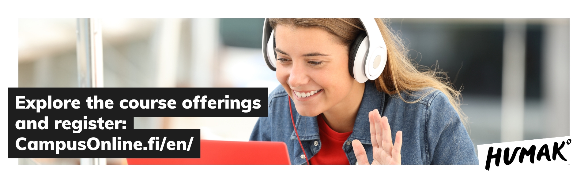 Nainen, jolla on valkoiset kuulokkeet, siittoo kädellään kohti läppärinsä ruutua hymyillen. 