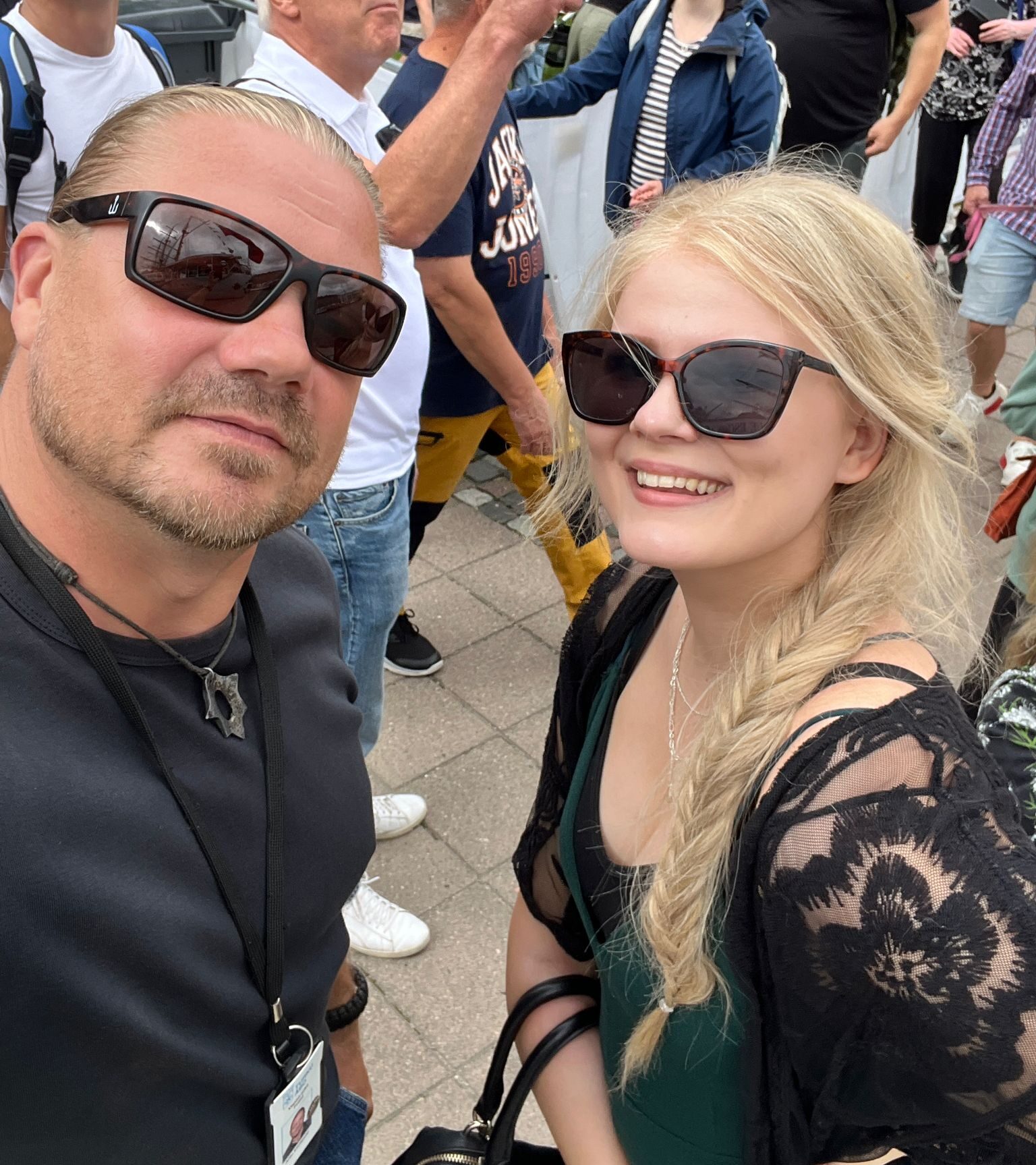 Kuvassa pariselfie aurinkolasisista miehestä ja naisesta, taustalla ihmisiä.