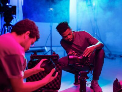 Kaksi henkilöä on kyykyssä lattialla ja katsovat kameroita.