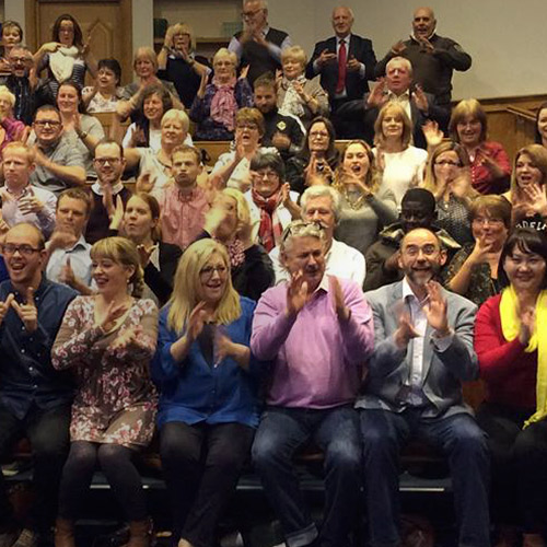 Yleisö istuu ja viittoo.