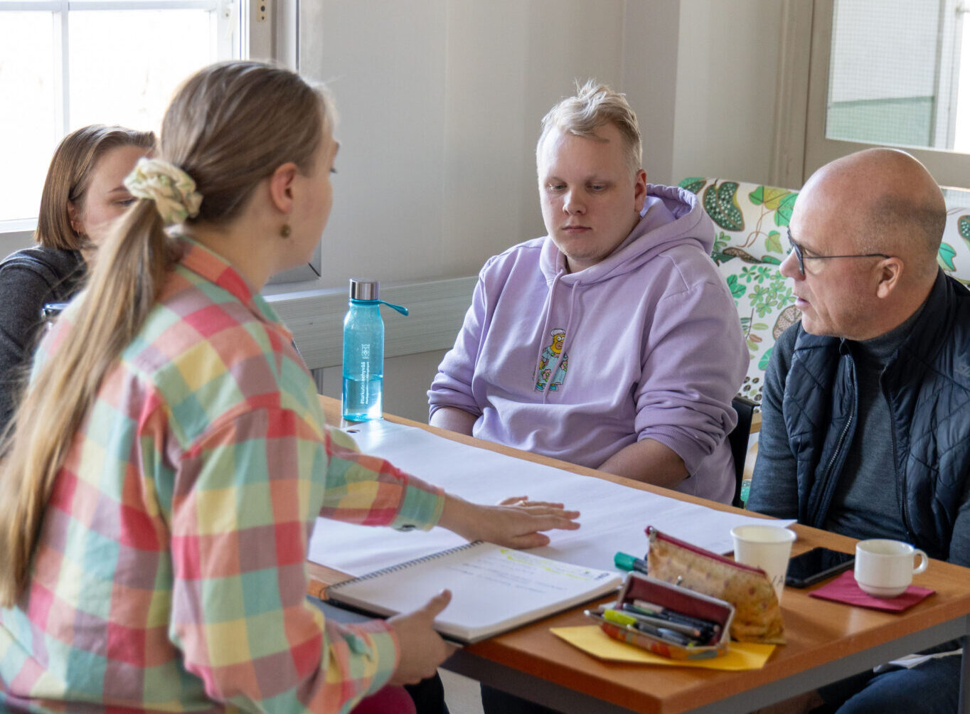 Kuvassa neljä ihmistä pöydän ympärillä pohtimassa jotain, pöydällä papereita.