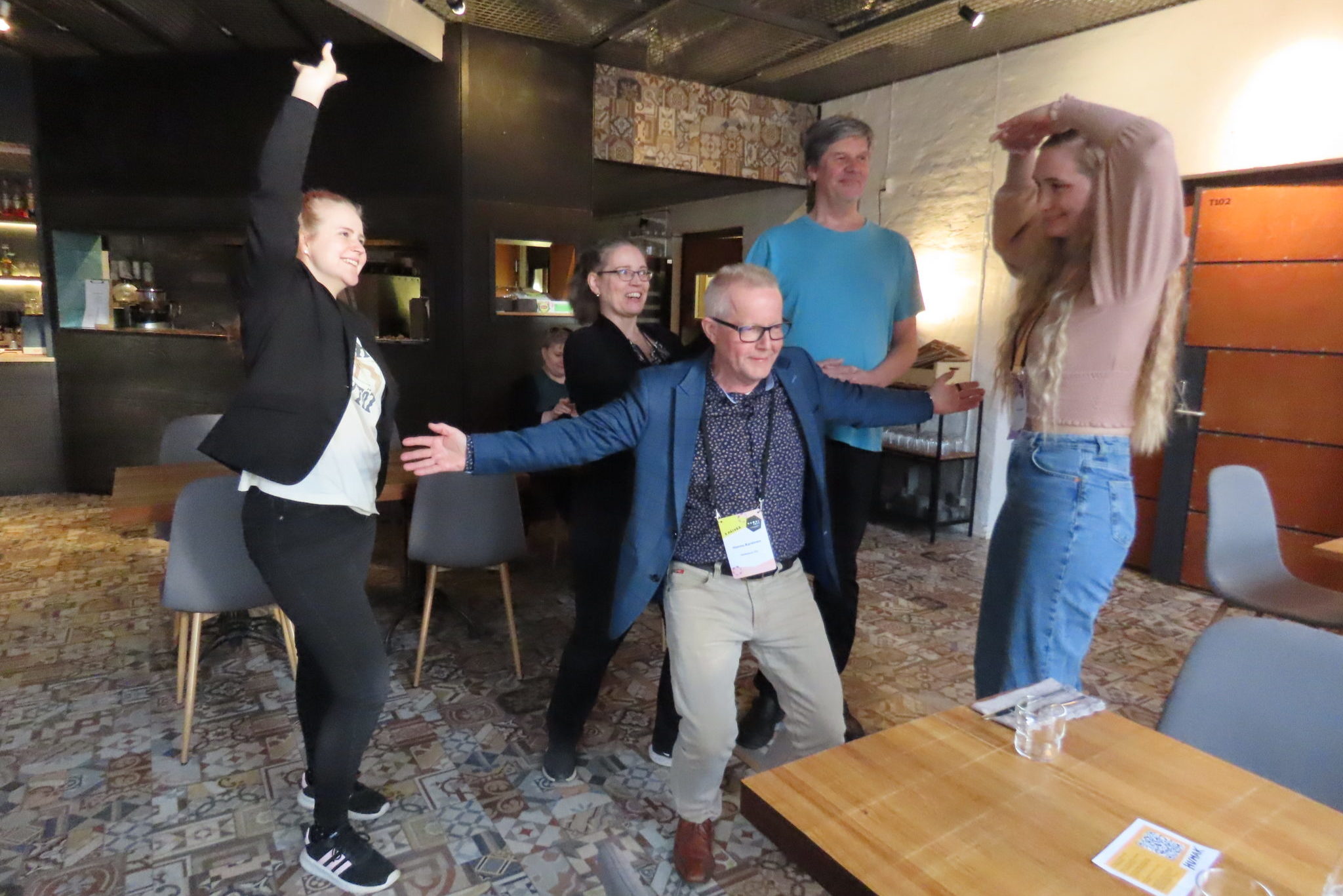 Viisi ihmistä tekee improa ravintosalissa ja he ovat erilaisissa hassuissa asennoissa.