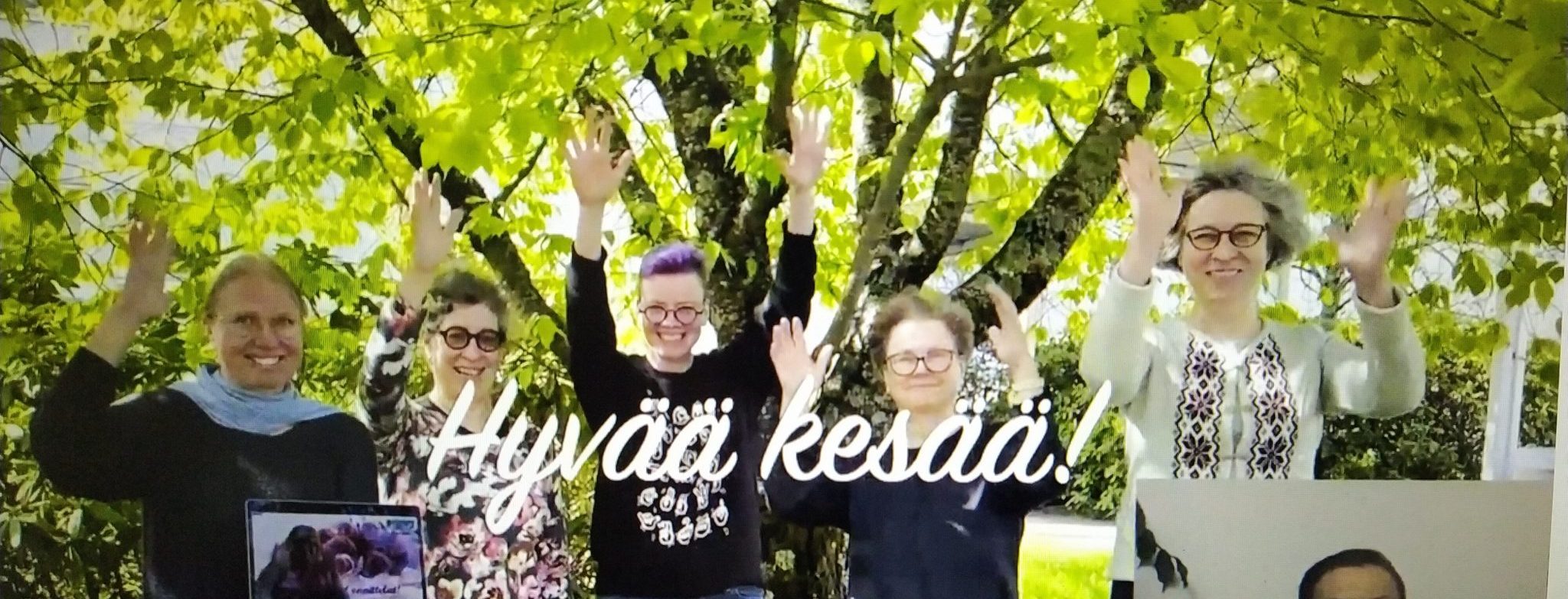 Ryhmä naisia seisoo rinnakkain kädet ylöspäin heiluen tervehdystä, taustalla tiuha lehtipuu, yhden naisen sylissä on auki oleva kannettava tietokone.